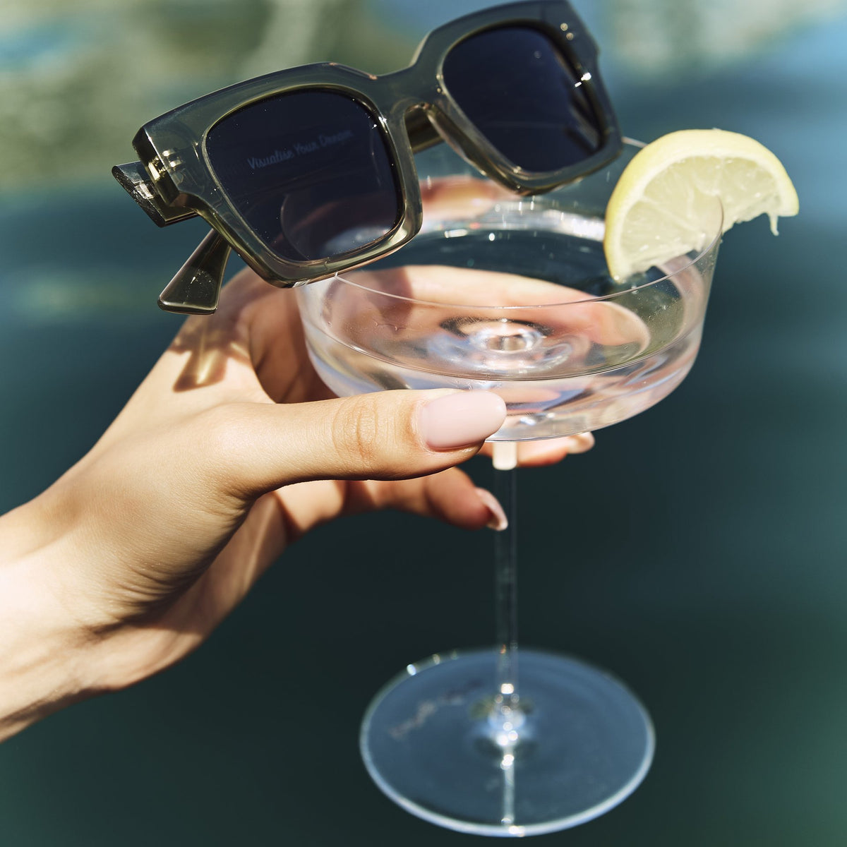 Celuna Olive sunglasses resting on a cocktail glass by the pool