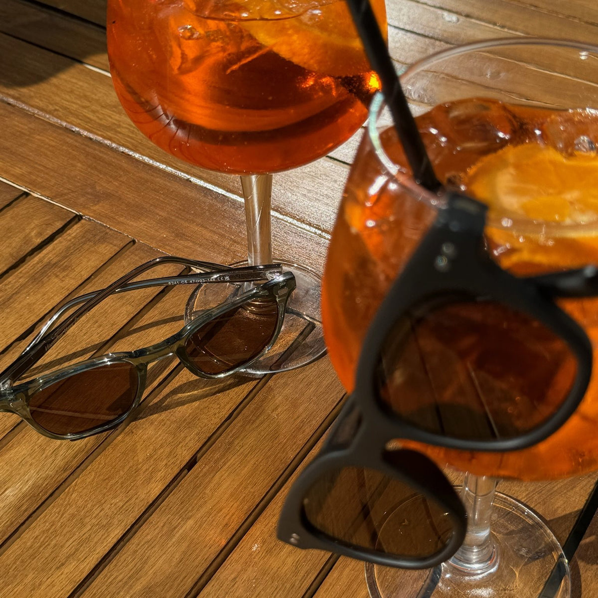 Lucid Green/Brown sunglasses on a wooden table next to Aperol spritz