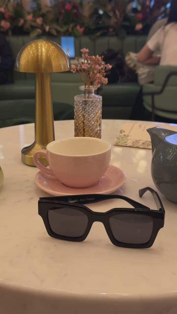 Celuna Black sunglasses on a marble café table with Visualise Your Dream engraved on the arm