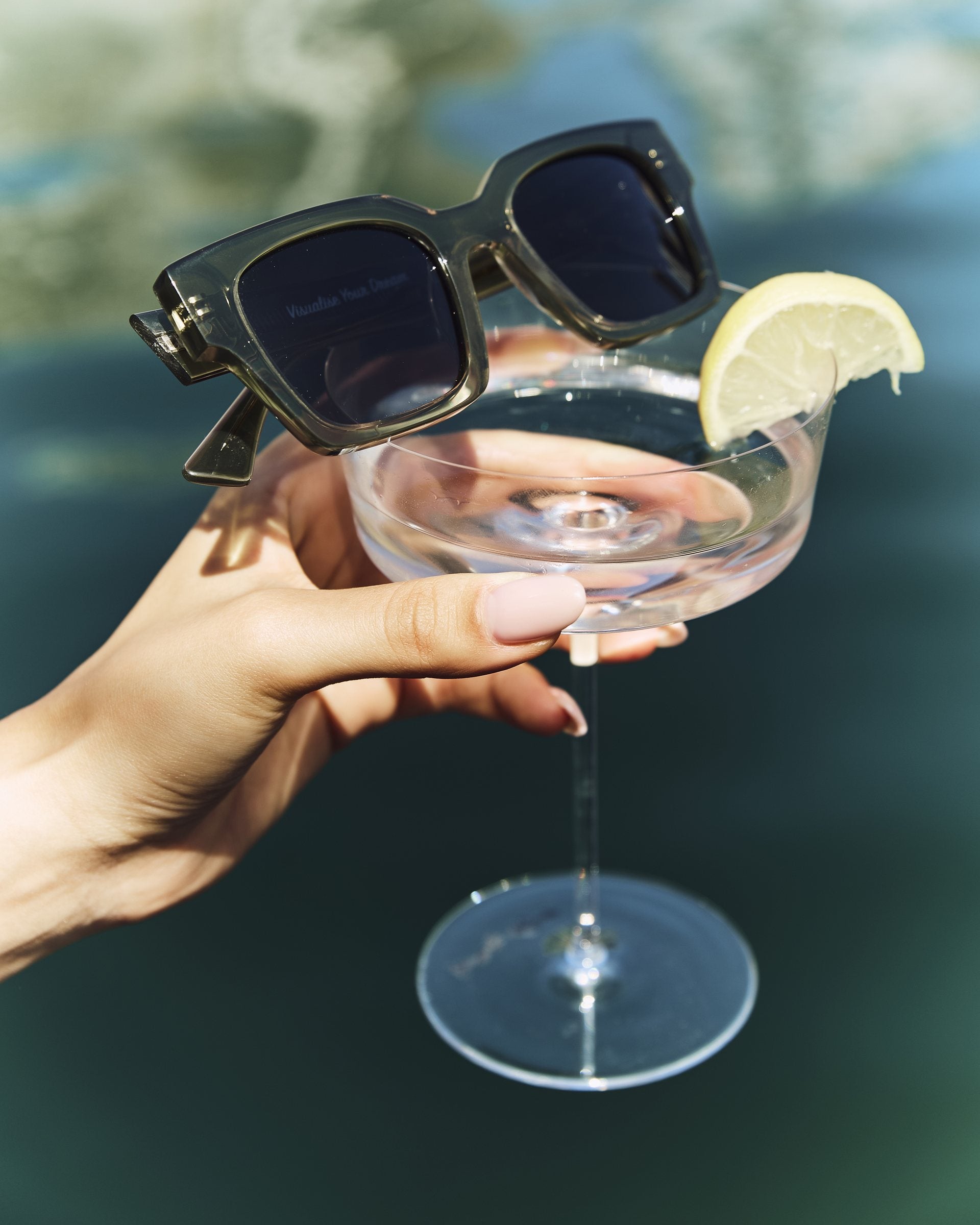 Celuna Olive sunglasses resting on a cocktail glass by the pool