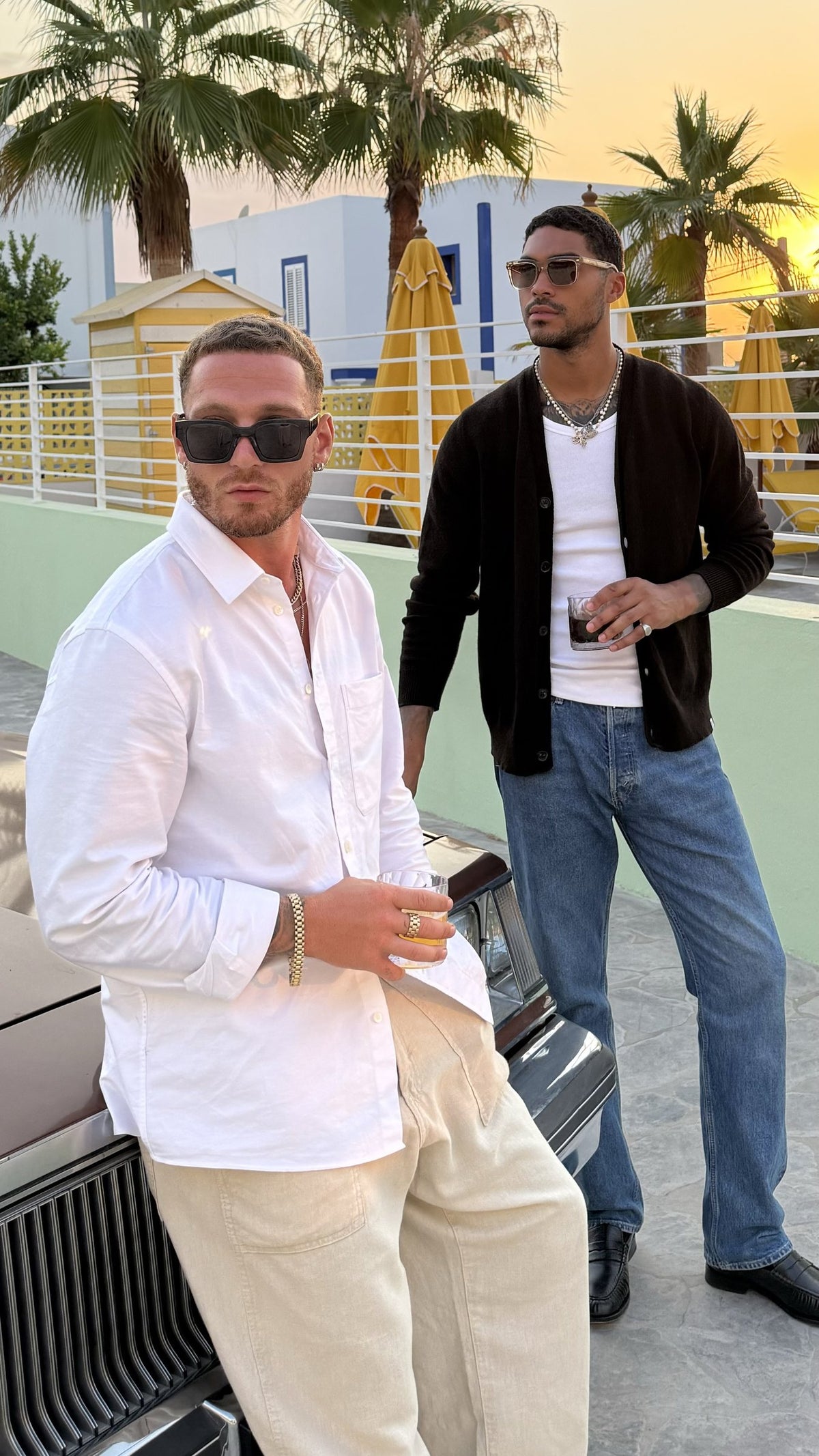 Two men in Yume sunglasses leaning on a vintage car at sunset