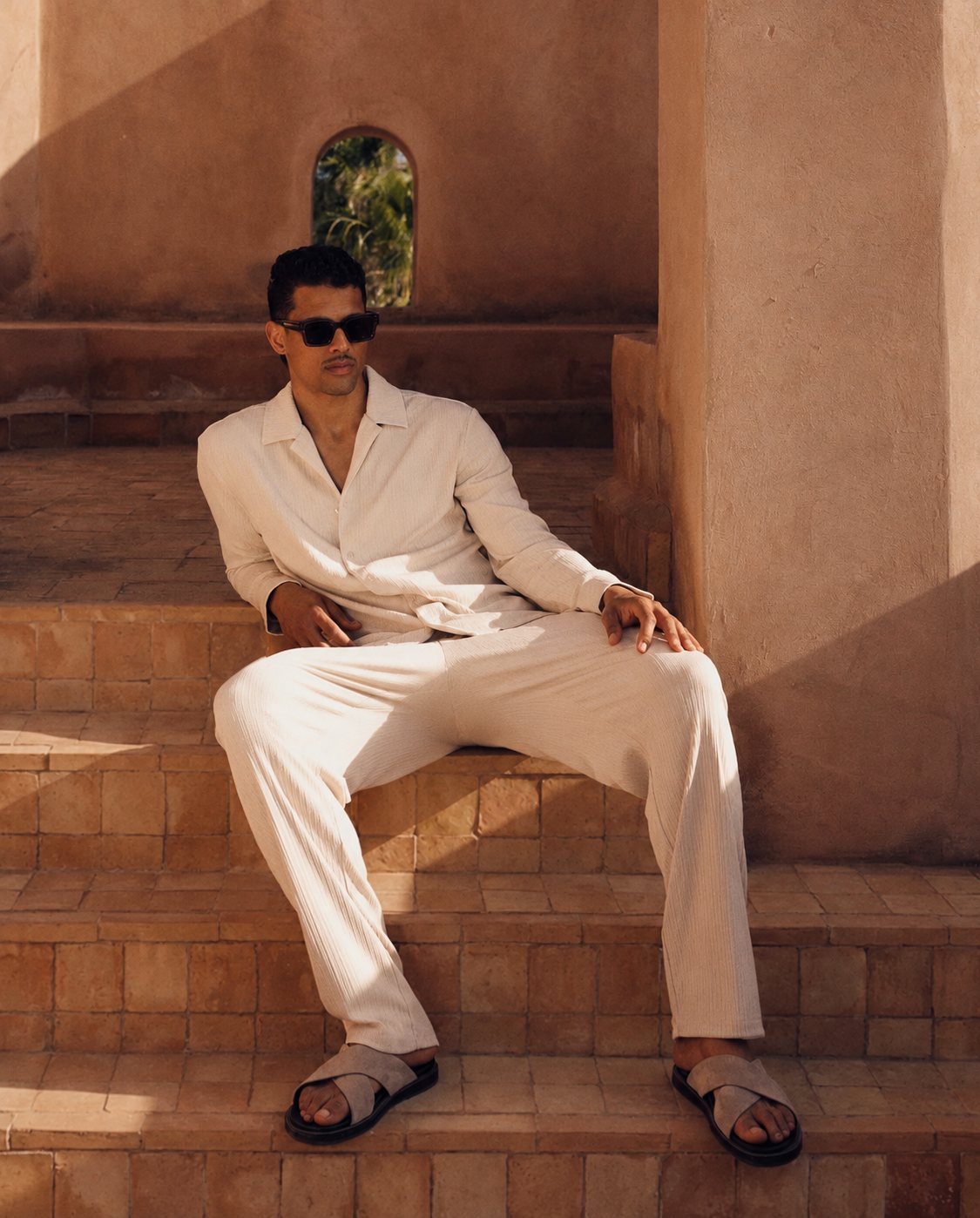 Man in cream linen wearing black Yume sunglasses on terracotta steps