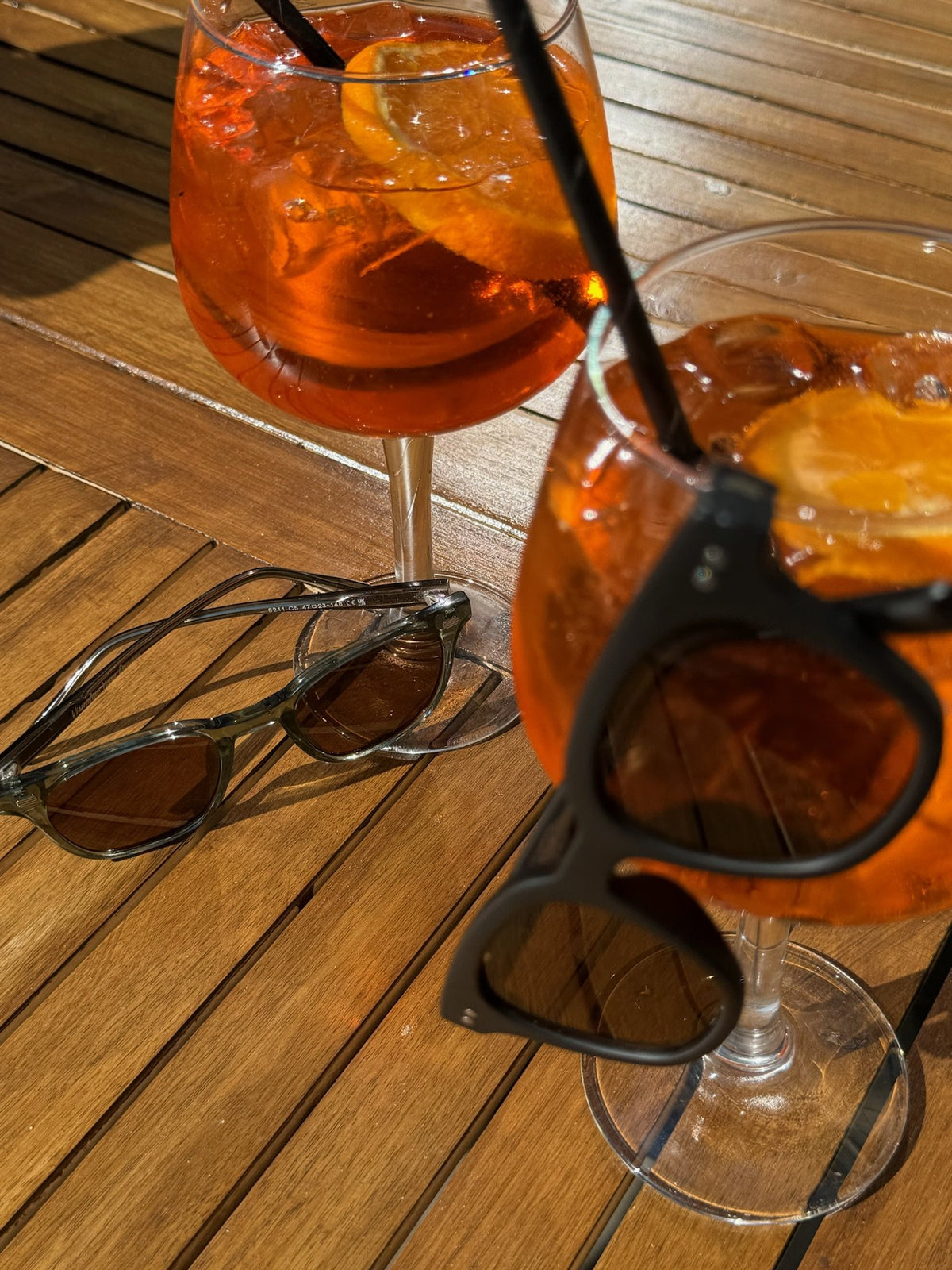 Lucid Green/Brown sunglasses on a wooden table next to Aperol spritz