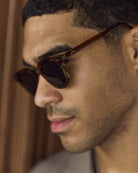 Close-up of a man wearing Noxie Brown/Green round sunglasses
