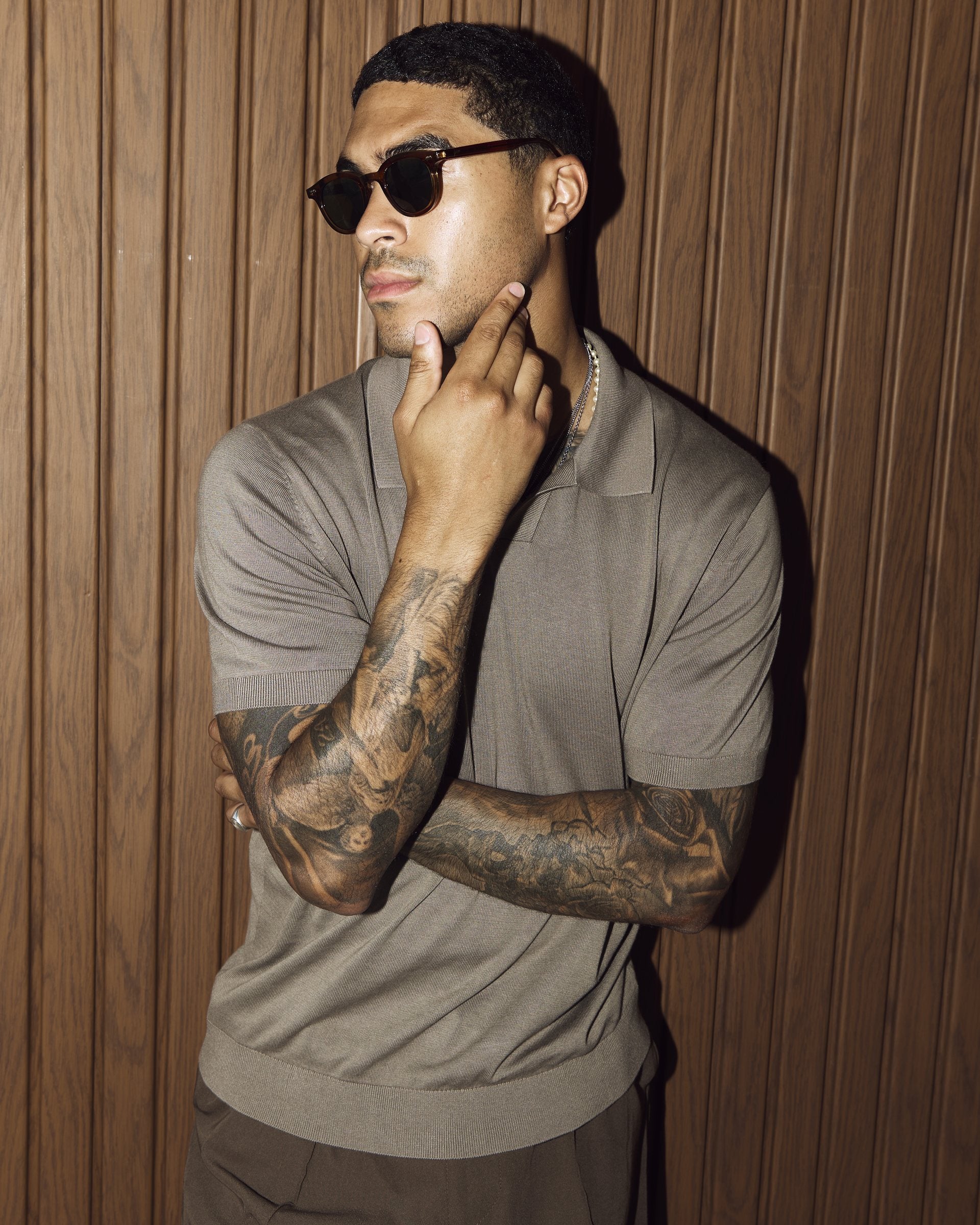 Man wearing Noxie Brown/Green sunglasses against a wooden wall