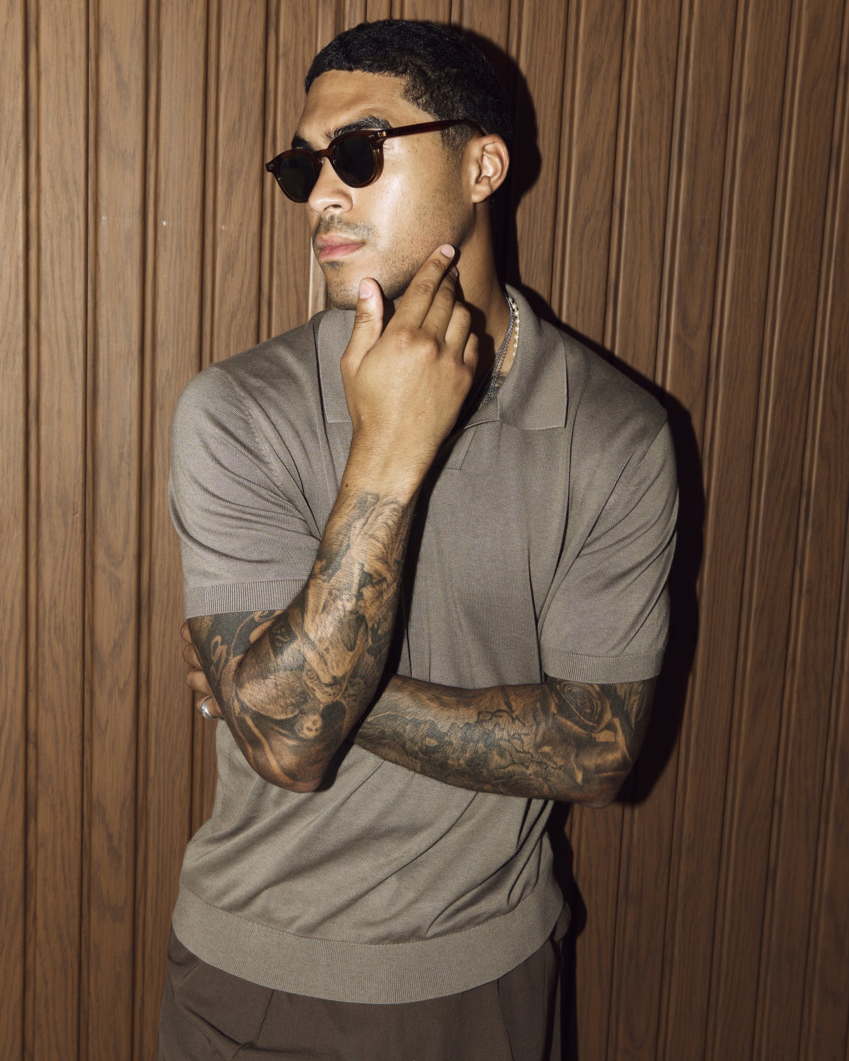 Man wearing Noxie Brown/Green sunglasses against a wooden wall